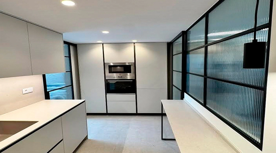 Cerramiento de aluminio negro y vidrio para separar cocina y salón con estilo.